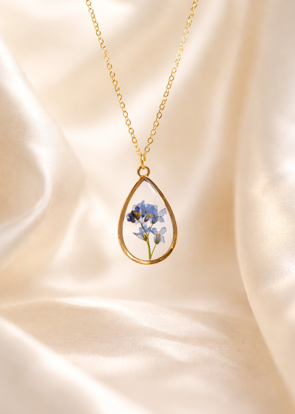 Gold necklace with a teardrop-shaped pendant featuring dried flowers on a soft beige fabric background