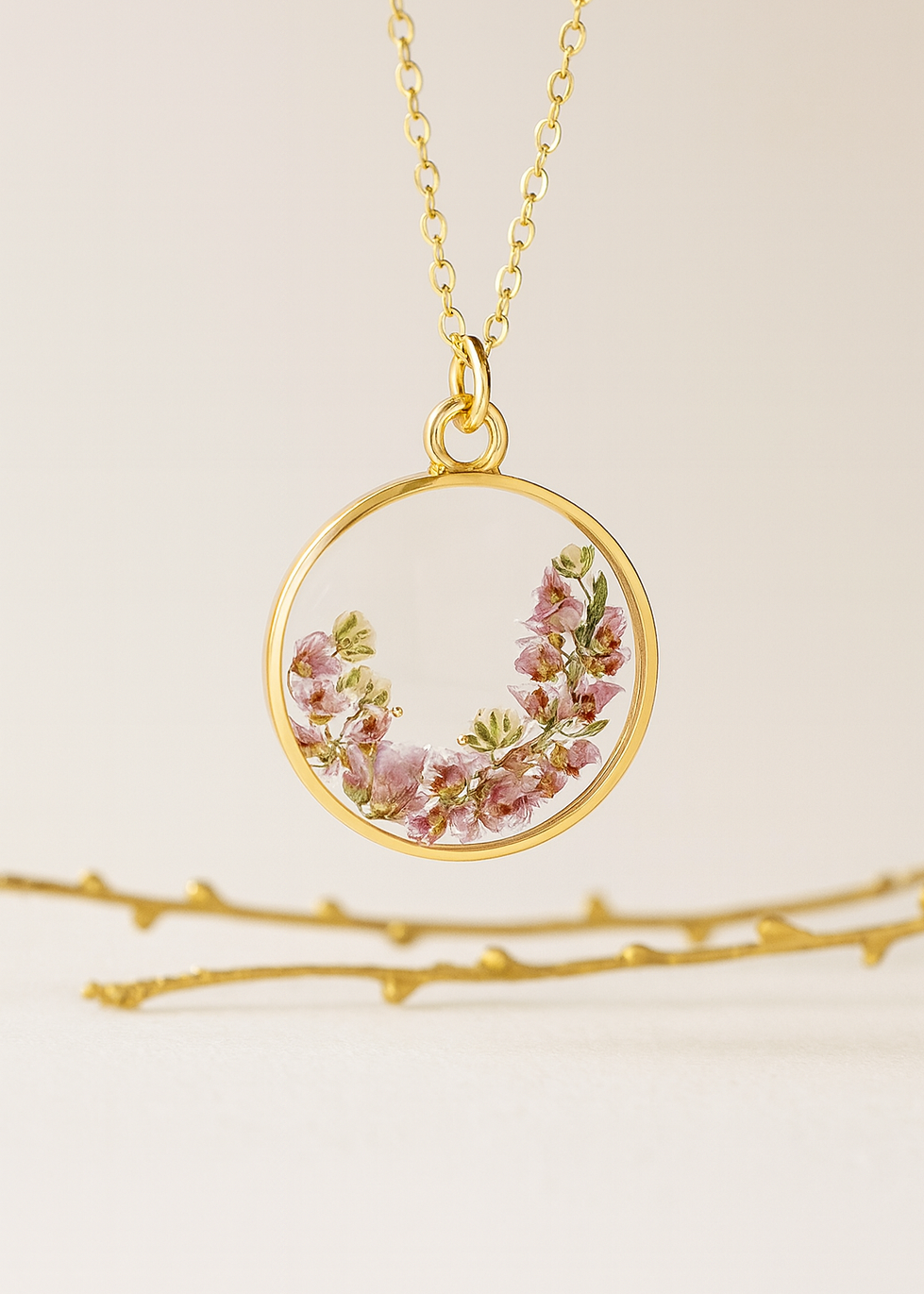 Gold necklace with a circular pendant featuring pink flowers on a beige background resin flower necklace with real dried flowers