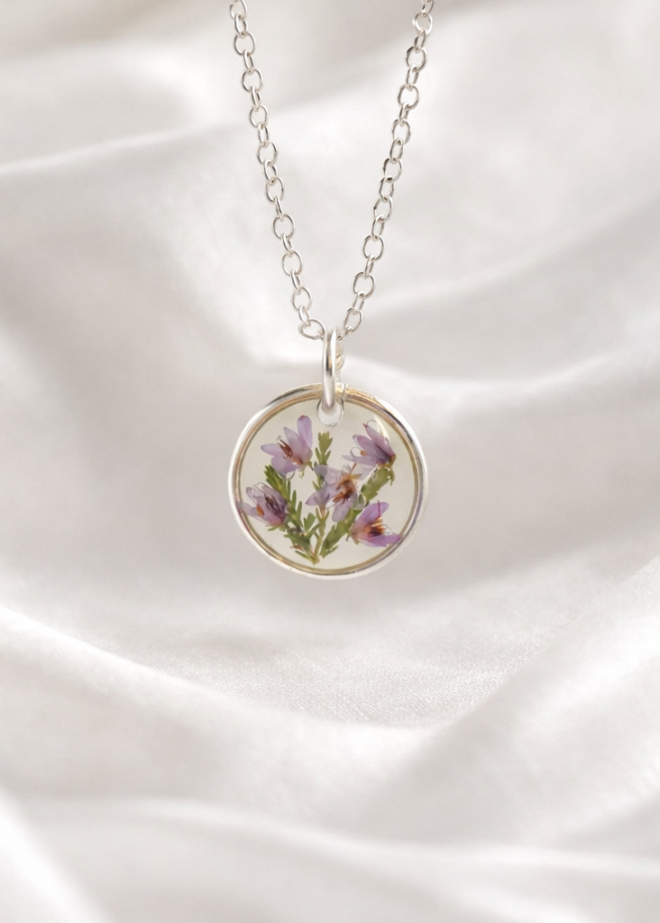 Silver necklace with a round pendant featuring purple flowers on a white fabric background