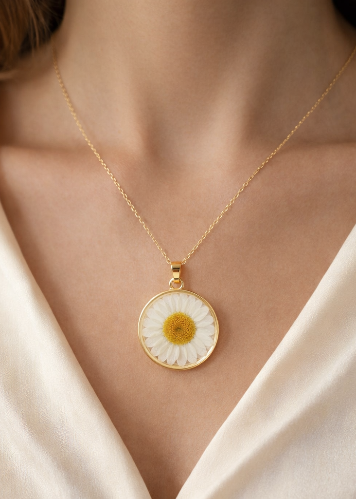 Gold necklace with a daisy pendant worn by a person in a white outfit.